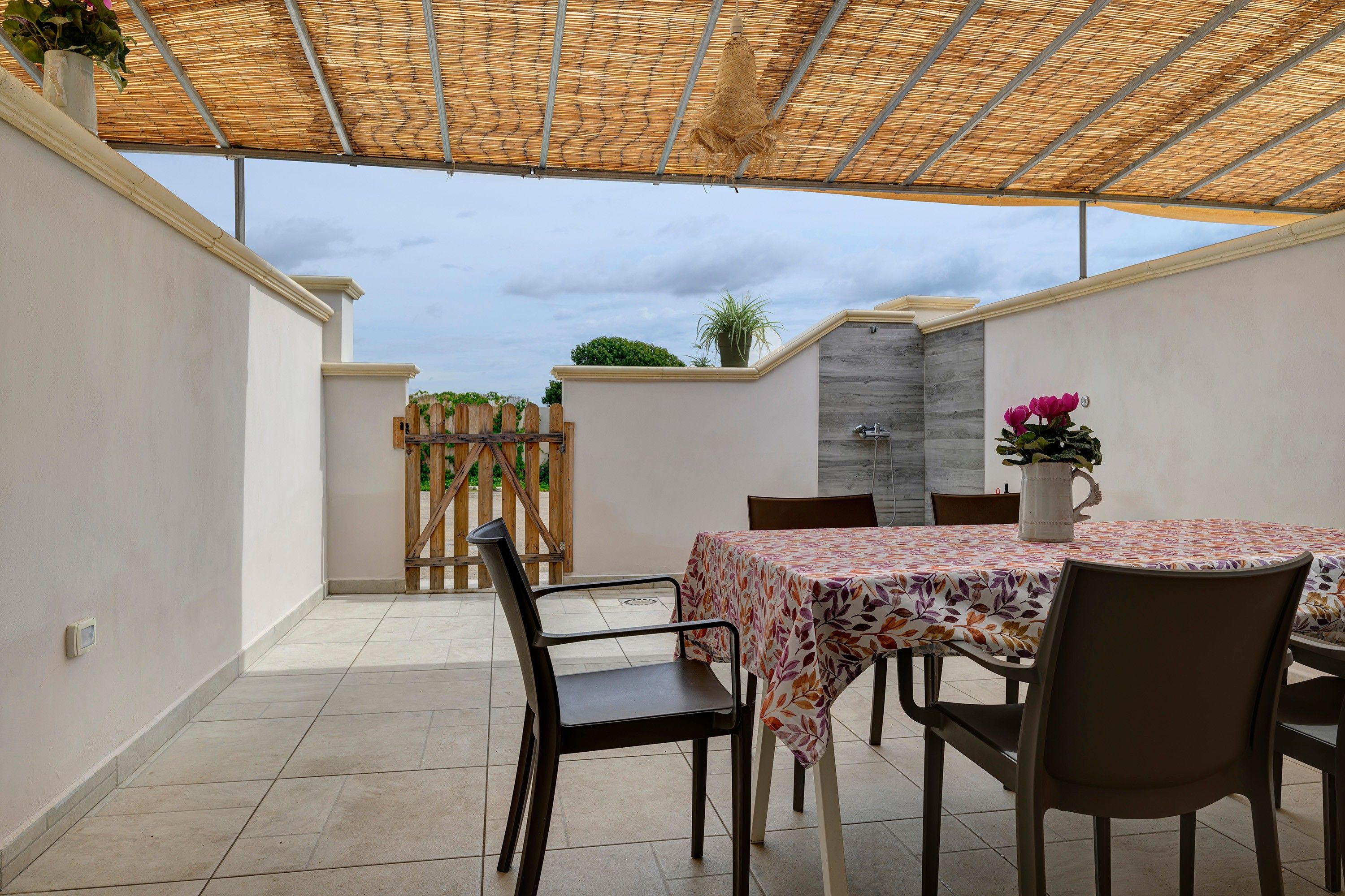 Eine Terrasse im Freien mit Tisch und Stühlen, ein überdachter Bereich mit einem gewobenen Dach und Blick zum Himmel.