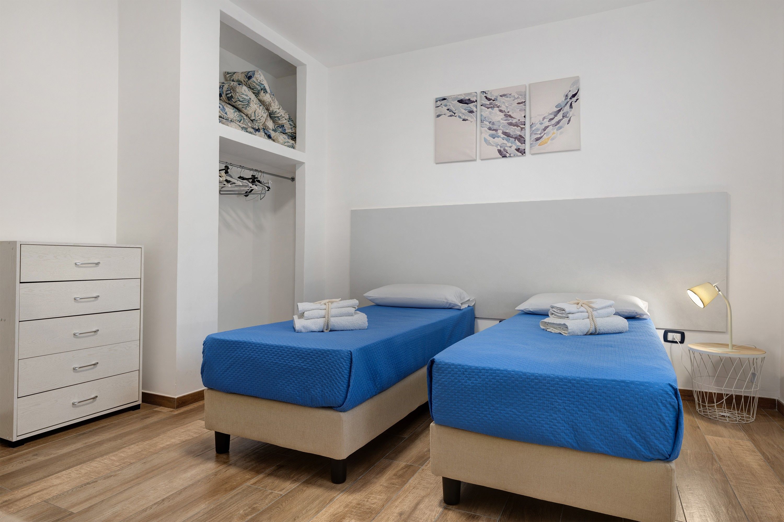 A hotel room with two beds, a wardrobe, a hanging wardrobe, and a bedside table with a lamp.