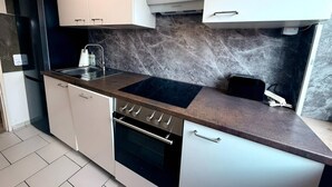 Moderni keittiö, jossa on valkoiset kaapit, musta työtaso ja sisäänrakennettu uuni.