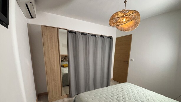 A bedroom with a bed, a wardrobe, a mirror, and a hanging light fixture. - Very comfortable, bright T3 in a quiet location with a beautiful exterior. (Occhiatana)