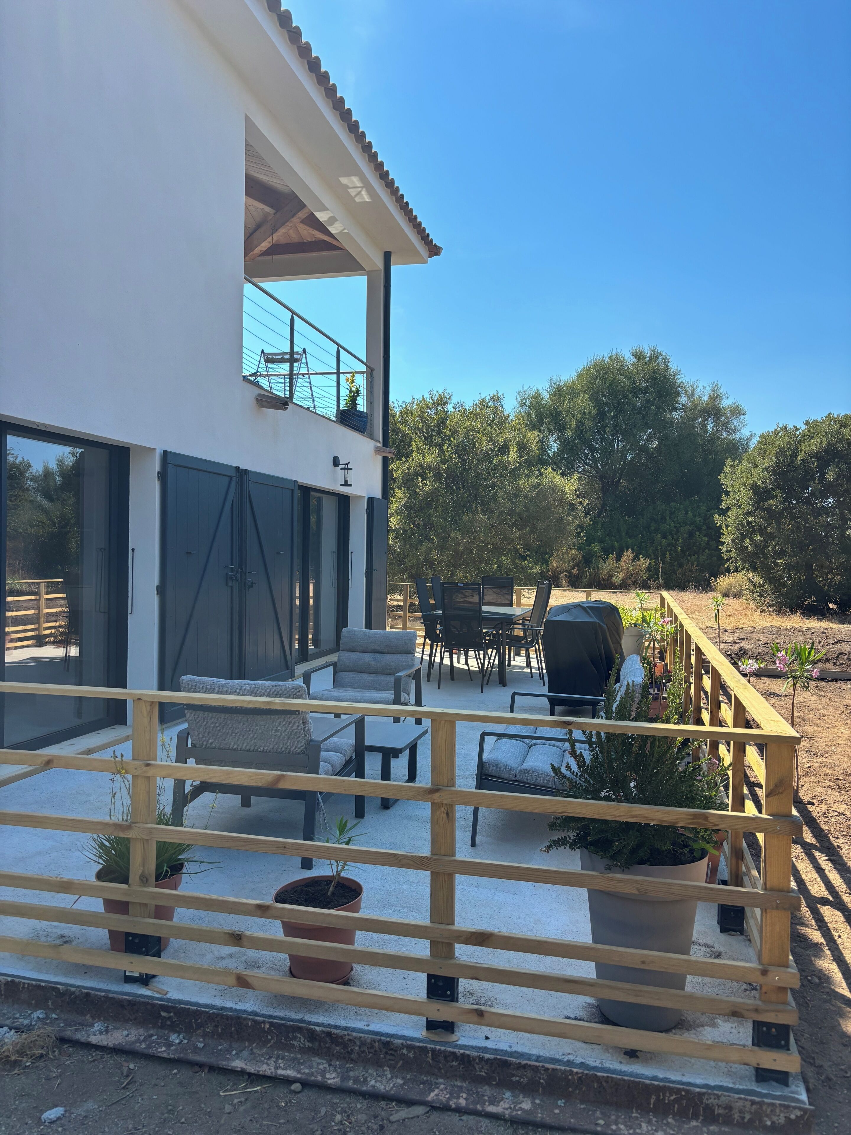 Ein modernes Haus mit überdachter Terrasse, Sitzgelegenheiten im Freien und Blumentöpfen.