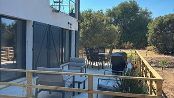 Ein modernes Haus mit überdachter Terrasse, Sitzgelegenheiten im Freien und Blumentöpfen.