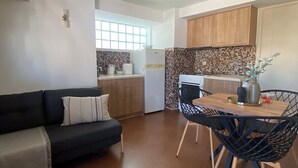 Een ruimtelijk ingerichte leefruimte met een bank, eettafel, stoelen en een keuken voorzien van kasten en een koelkast.