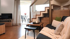 Een moderne woonkamer met een bank, salontafel, televisie en een trap naar een balkon.