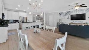 Uma cozinha moderna com armários brancos, uma ilha central e um espaço de refeições com mesa de madeira e cadeiras brancas.