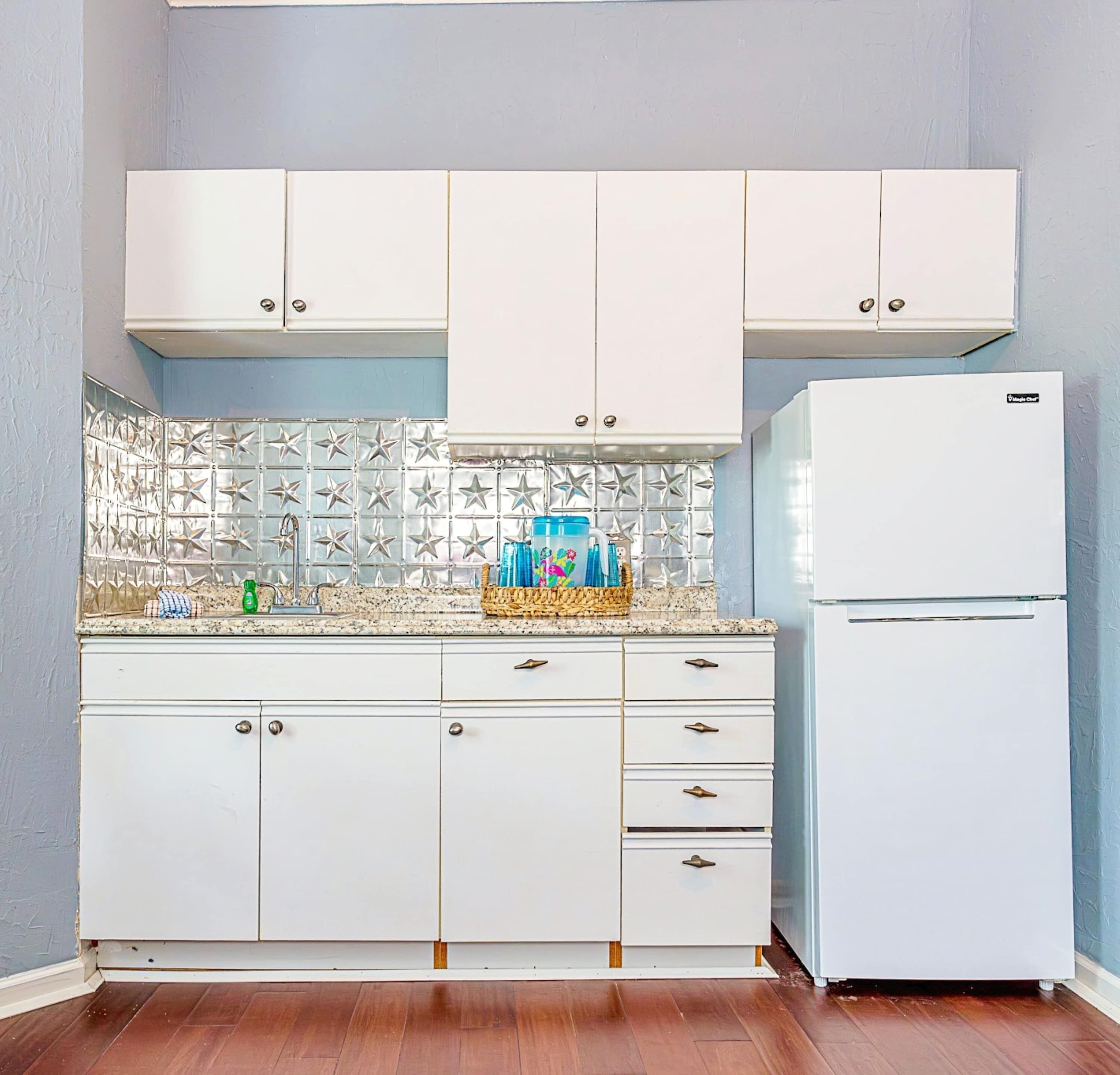 A kitchen with white cabinets, a refrigerator, and a tiled backsplash.
