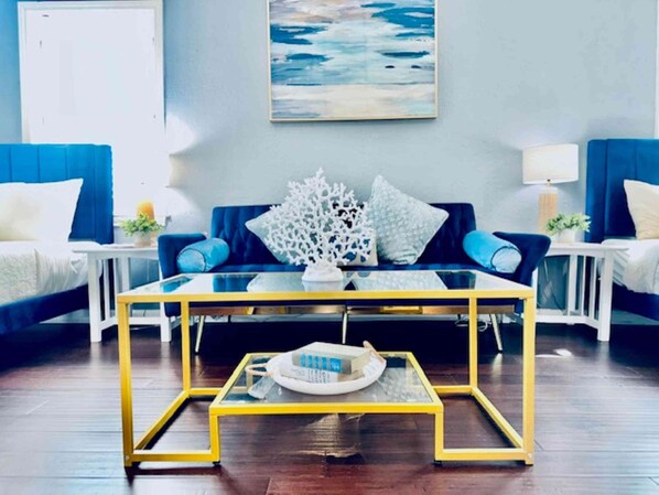 Un salon moderne avec une table basse en verre, des canapés bleus et un tableau accroché au mur.