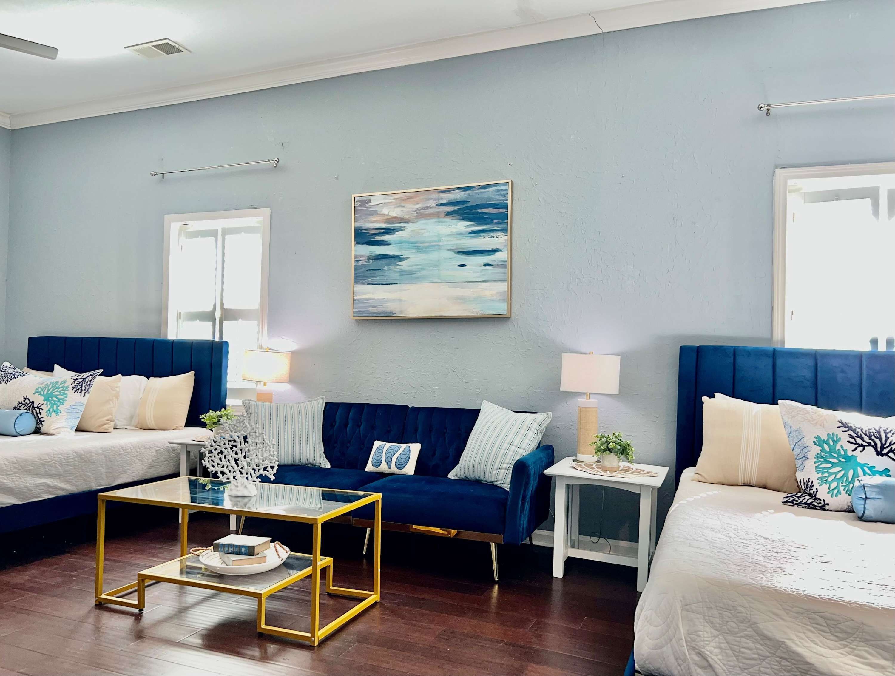 Une chambre d’hôtel moderne avec un canapé bleu, deux lits, une table basse en verre et un tableau au mur.