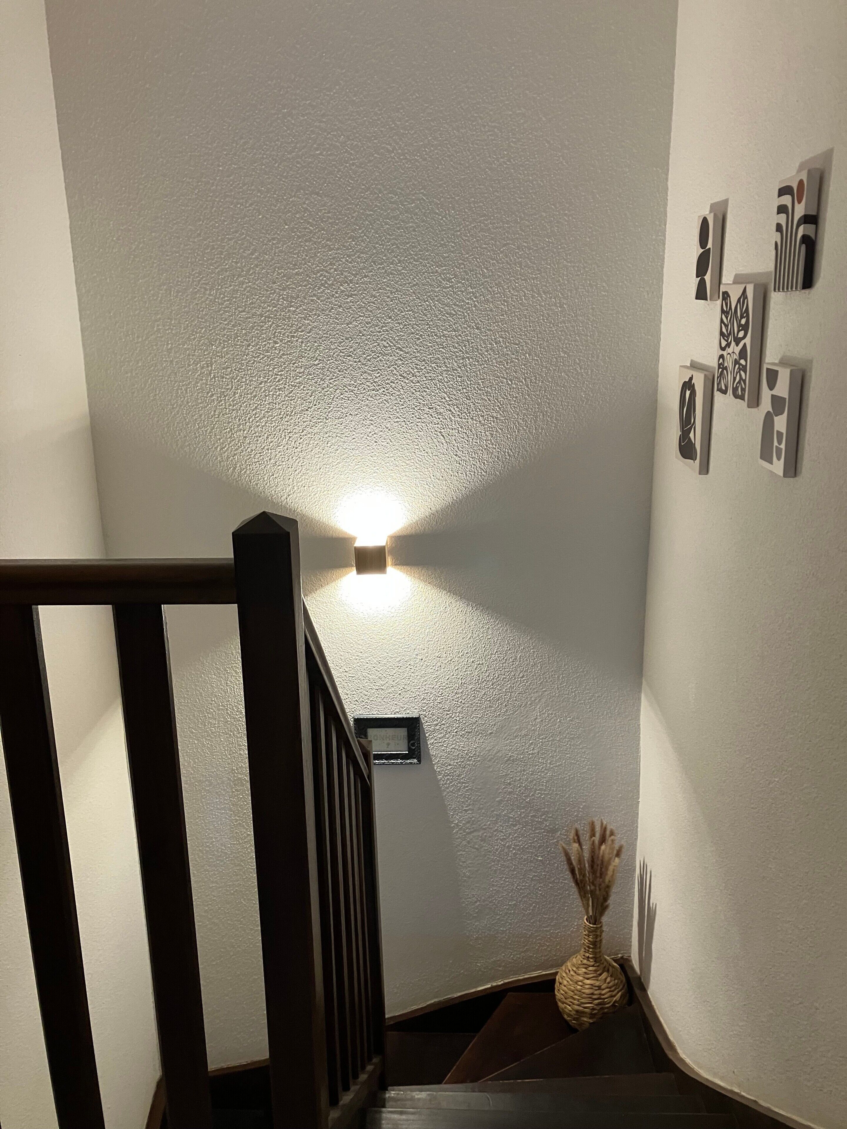 Een trap met een structuurwand, een wandlamp en een klein bordje.