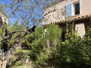 Un bâtiment doté d’un toit en tuiles, entouré de différents arbres et arbustes.