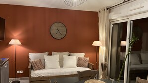 A bedroom with a bed, bedside lamps, a clock, a bedside table, and a view through a sliding door. - House in Drôme Provençale - Domaine de L'oliveraie (Nyons)