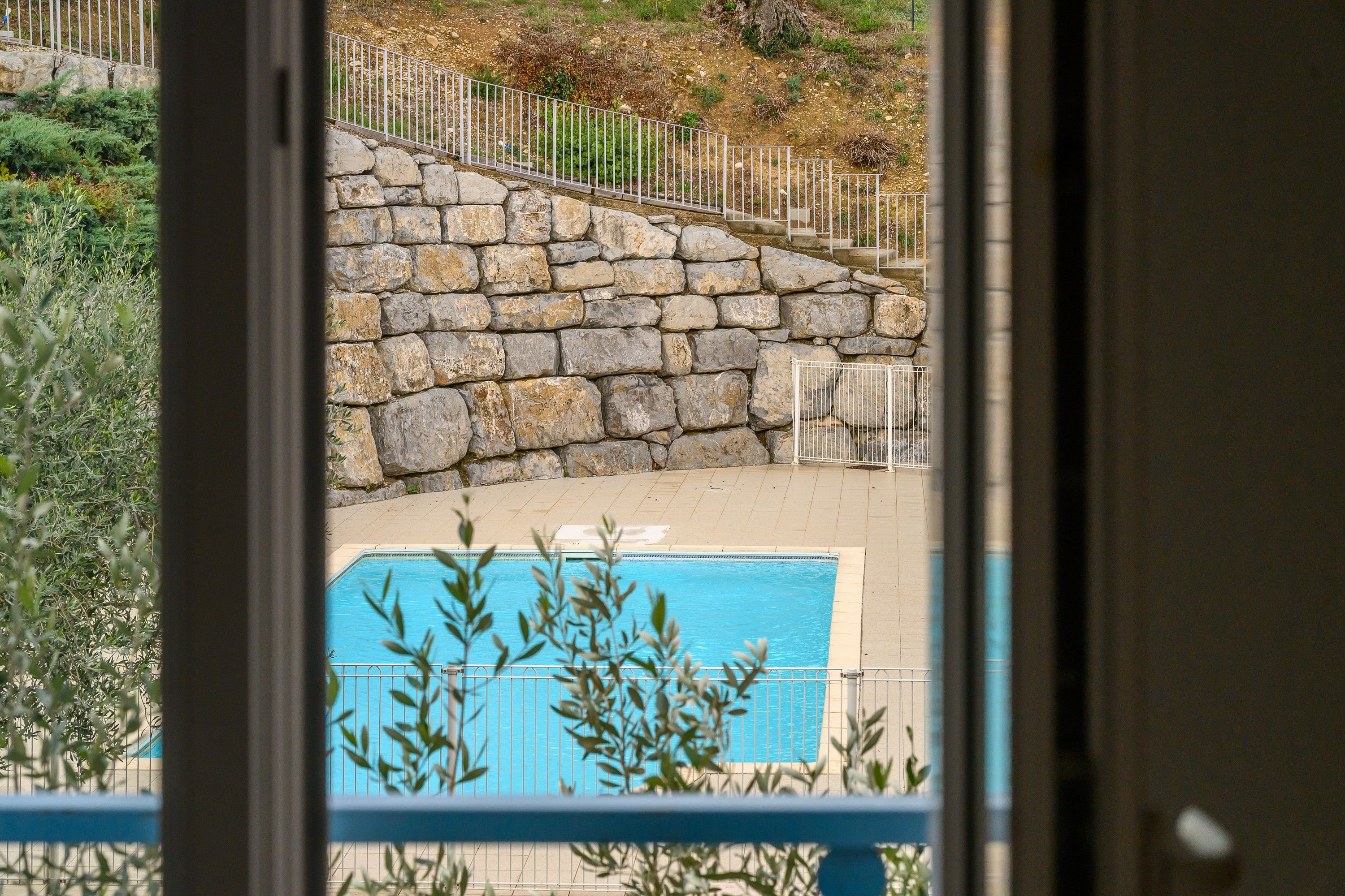 Una escalera de piedra lleva a un área de piscina con vistas a un edificio a través de un ventanal.