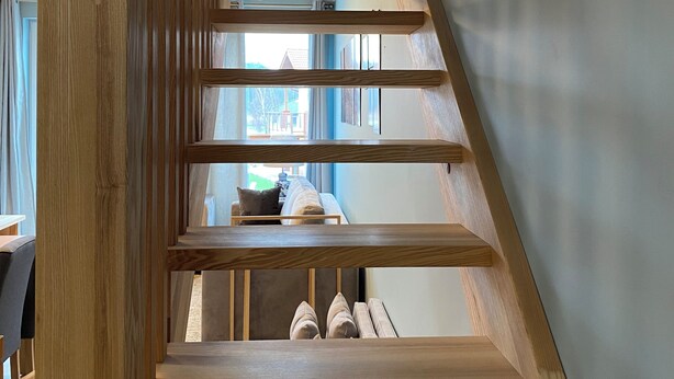 Eine Holztreppe mit Blick auf einen Wohnbereich oben.