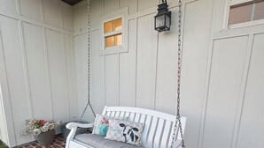 En vit veranda med en gungstol, en lykta och ett litet fönster.