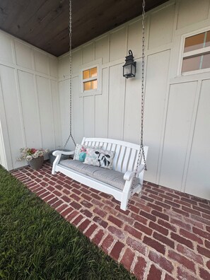 A white porch with a swing seat, a lantern, and a small window.