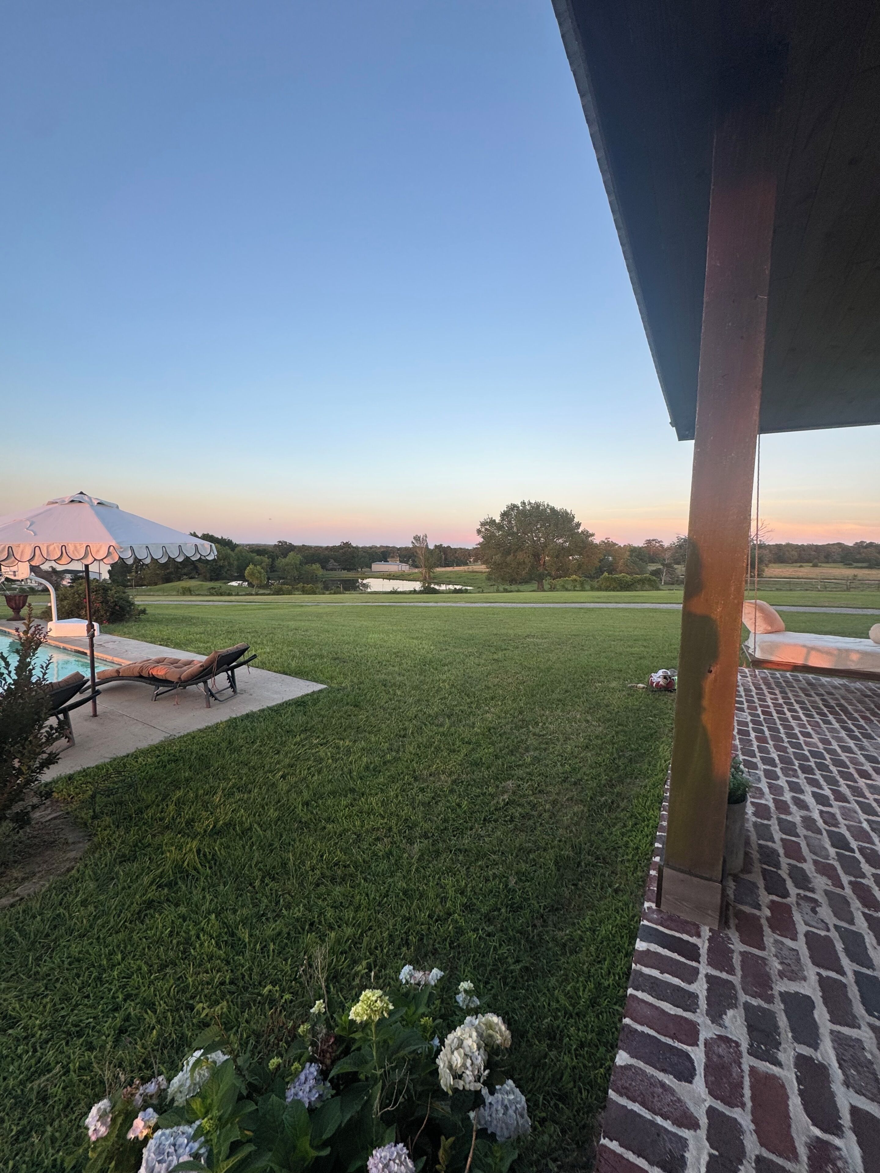 A grassy yard with a pool, lounge chairs, and a brick patio.