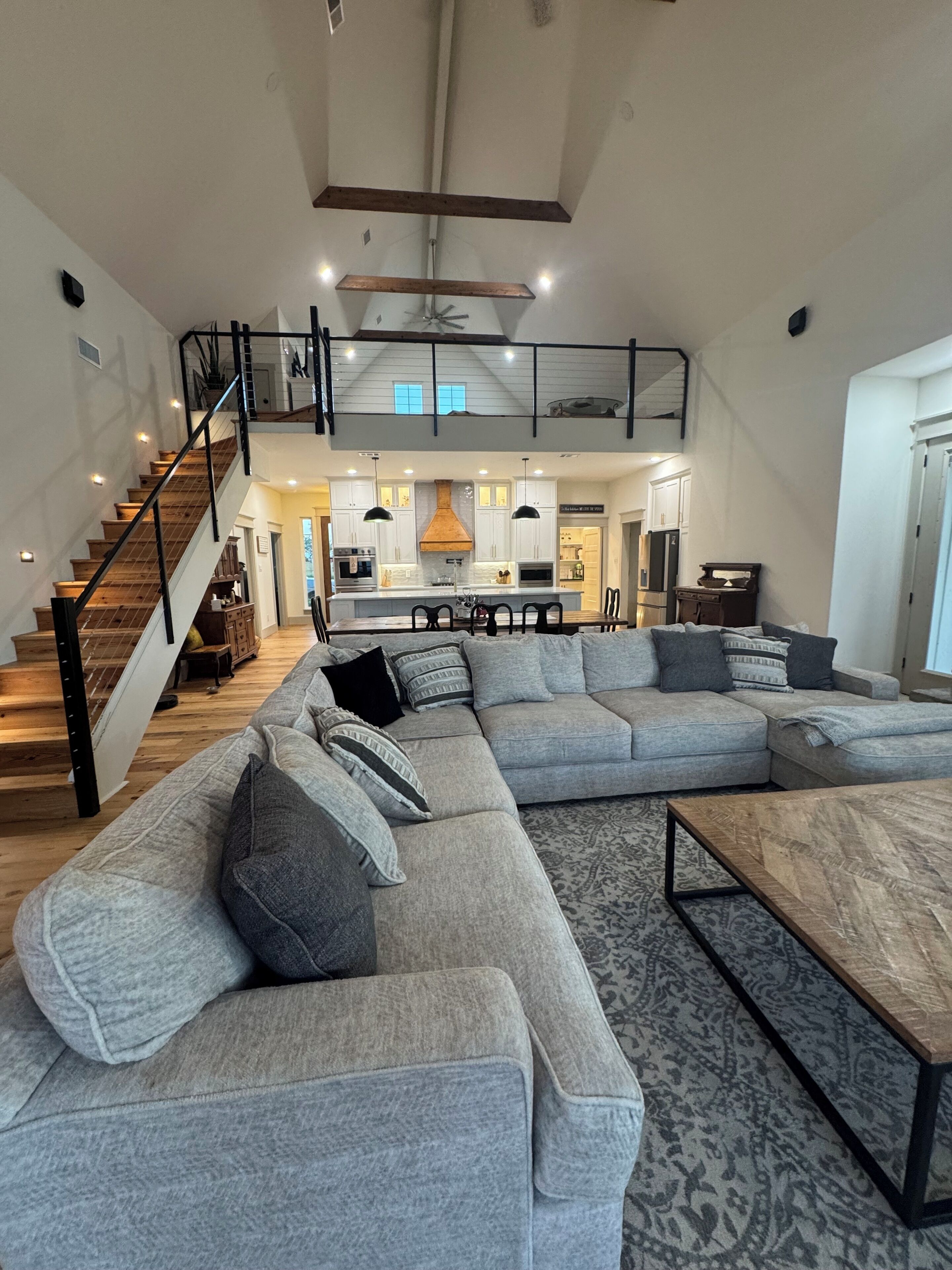 A spacious living area with a large sectional sofa, a wooden coffee table, and a staircase leading to an upper level.