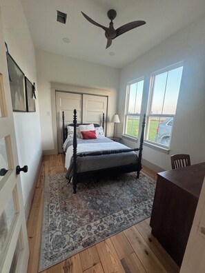 A bedroom with a four-poster bed, a ceiling fan, a large window, and a view of the outdoors.