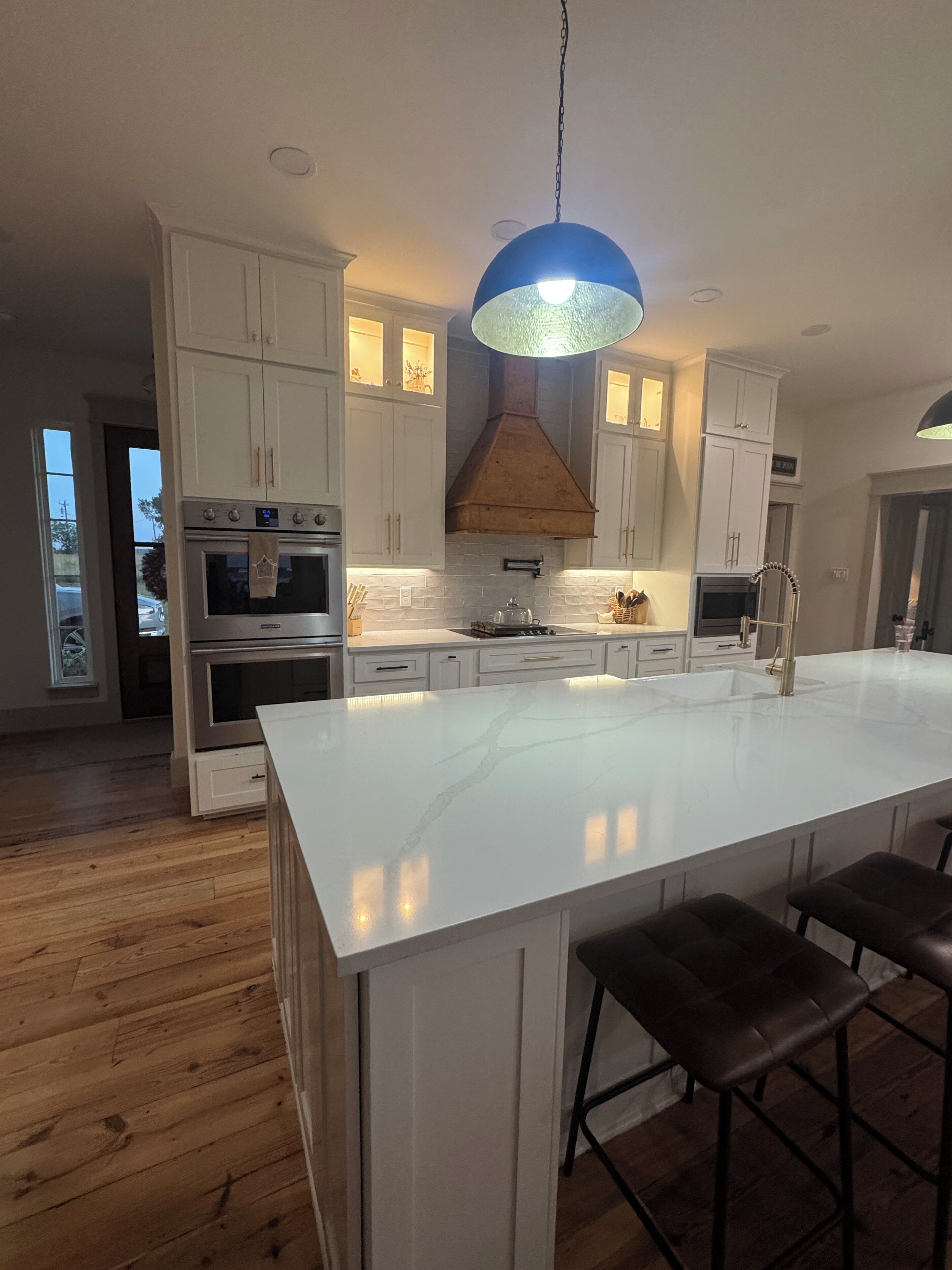 A modern kitchen with white cabinetry, a large island with bar stools, and a blue pendant light.