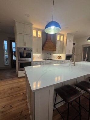 A modern kitchen with white cabinetry, a large island with bar stools, and a blue pendant light.