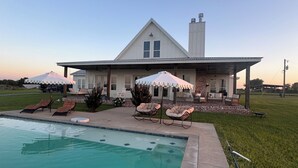 Ett hus med en swimmingpool, utomhusmöbler och en täckt uteplats.