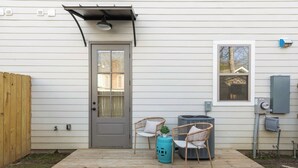 A wooden deck with two wicker chairs and a small table, a gray door, and a window with a view of a house.