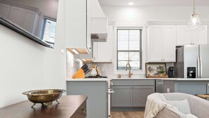 A modern kitchen with white cabinets, a wooden dining table, and a gray sofa.