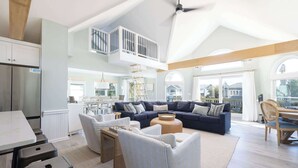 A spacious living area with a high ceiling, a built-in loft with a railing, a dark blue sofa set, and a dining area with a wooden table and chairs. - 5min to Beach w Resort Perks! Renovated CLR Home (Corolla)