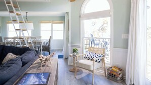 A spacious living room with a grey sofa, a wooden chair, a small table with a plant, and a ladder leading to a balcony. - 5min to Beach w Resort Perks! Renovated CLR Home (Corolla)