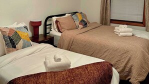 Hotelkamer met twee bedden, een plafondventilator, een raam met zonwering en een kunstwerk in een lijst aan de muur.