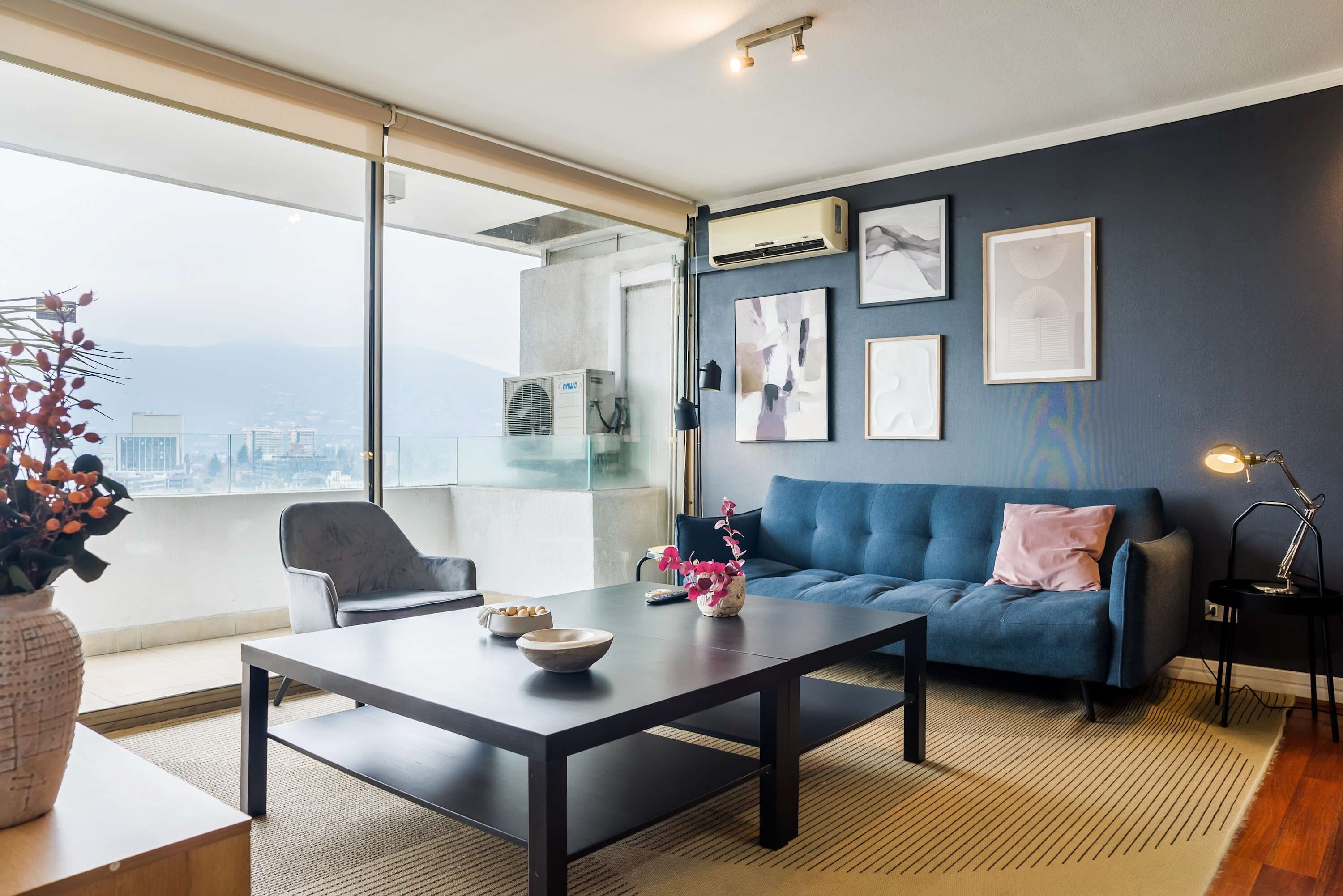 Ein modernes Wohnzimmer mit einer Couch, einem Couchtisch und Blick auf die Stadt durch große Fenster.