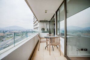 A balcony with a table and chairs, a view of a cityscape and mountains, and a large window. - Spacious 2 Bedroom Apartment with Pool and Gym! (Las Condes)