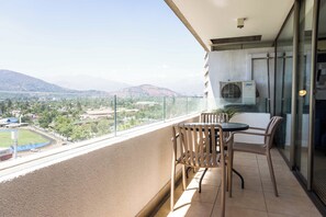 Un balcon avec une table et des chaises, offrant une vue sur le paysage urbain et les montagnes.