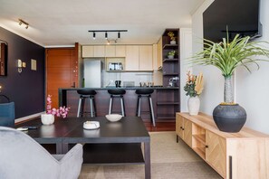 A modern kitchen with a central island, bar stools, and a dining table with a vase of flowers. - Spacious 2 Bedroom Apartment with Pool and Gym! (Las Condes)