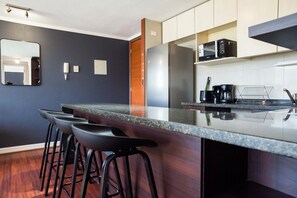 Une cuisine moderne avec un mur de couleur sombre, un comptoir-bar avec des tabourets, un four à micro-ondes et une machine à café.