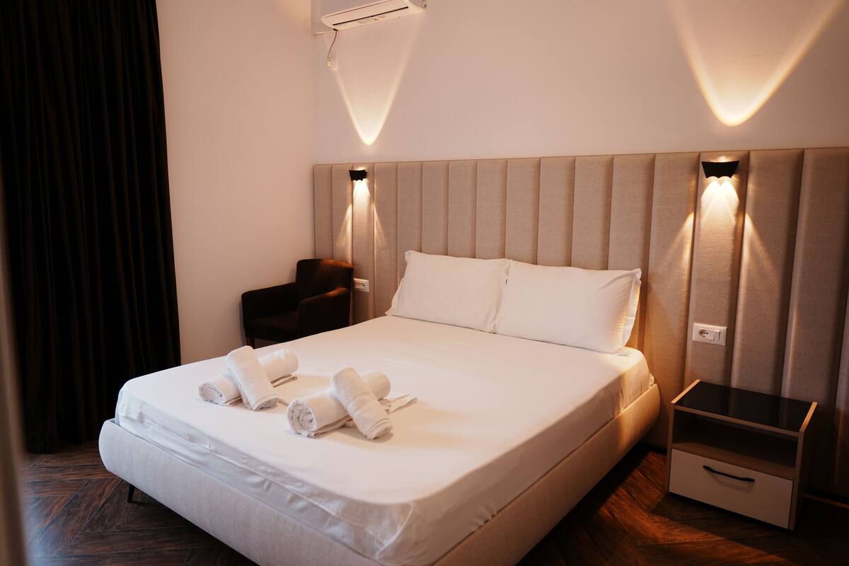 Una habitación de hotel con una cama grande, dos mesitas de noche y un aire acondicionado instalado en la pared.