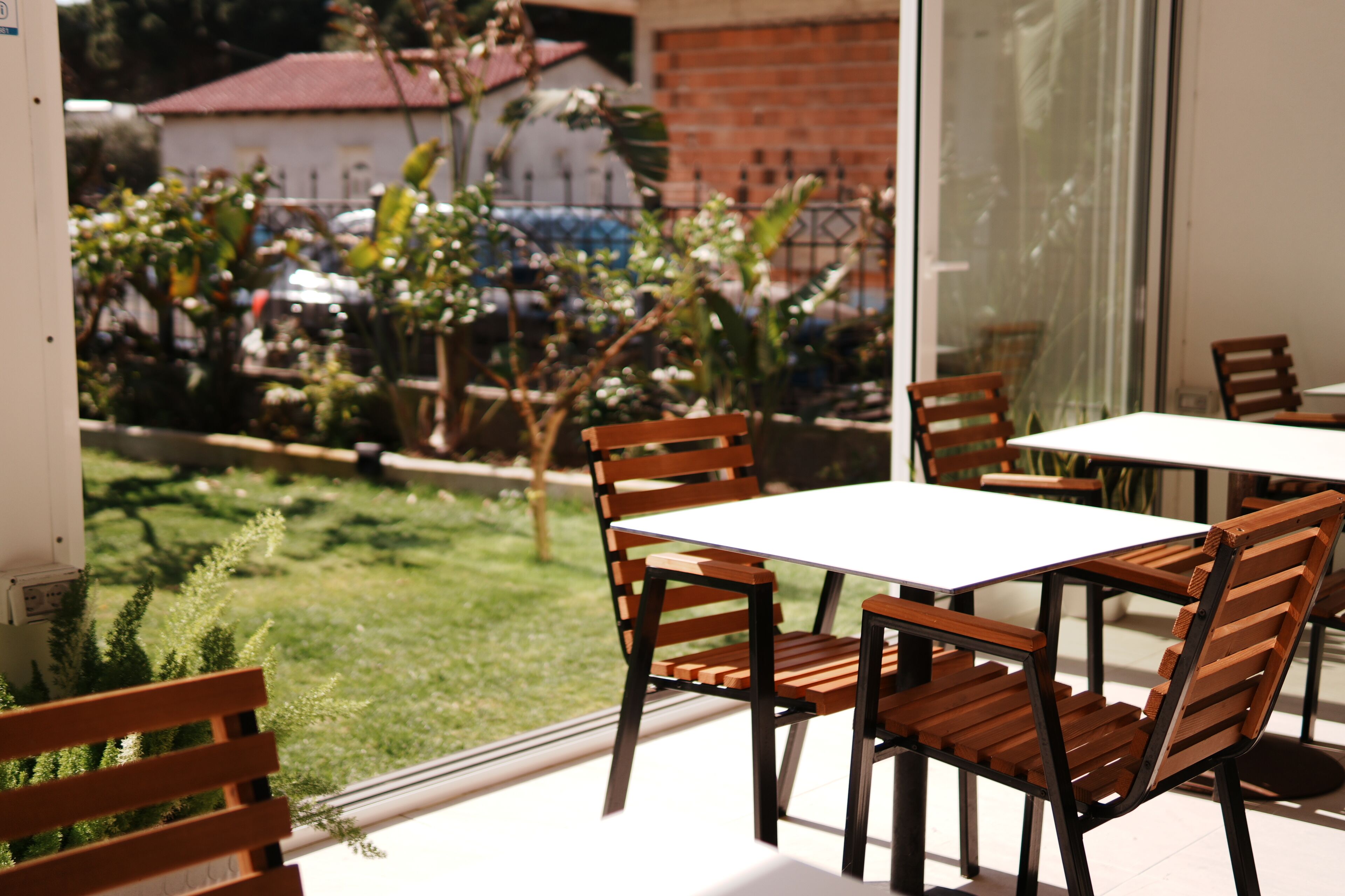 Un espace extérieur aménagé pour les repas, avec des tables et des chaises, une pelouse et une vue sur une rue bordée de voitures garées et d’immeubles.