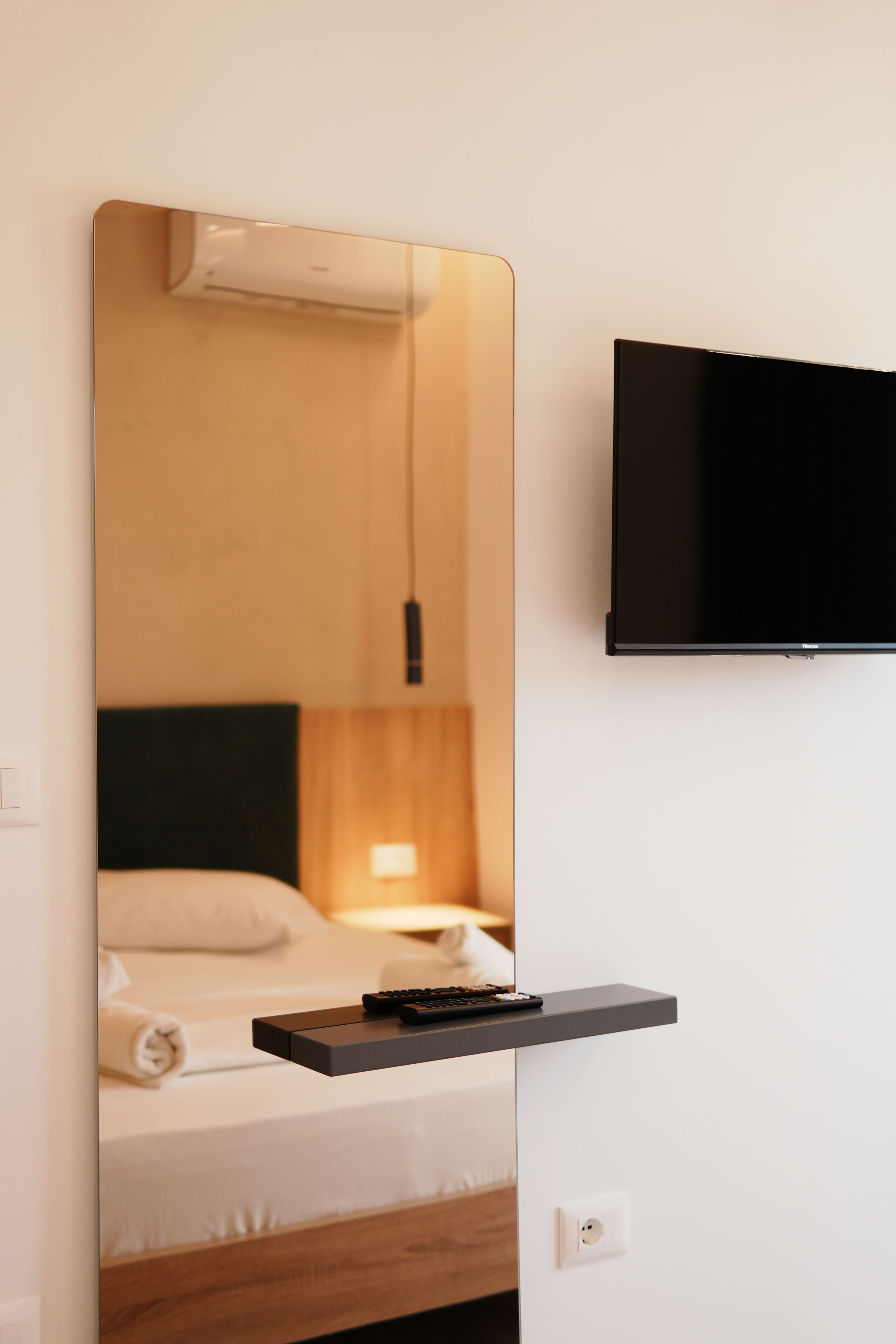 Une chambre d’hôtel moderne équipée d’un lit, d’un téléviseur fixé au mur et d’une table de chevet avec une télécommande.
