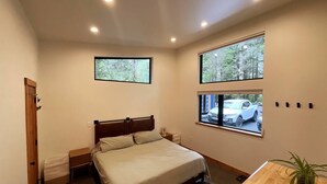 A bedroom with a bed, two windows, a wooden door, and a small table with a plant. - The Alpenglow: Waterfront Escape Private Hot Tub (Juneau)