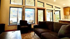A living room with a sofa, armchairs, and a coffee table. There are large windows with a view of mountains and a lake. - The Alpenglow: Waterfront Escape Private Hot Tub (Juneau)