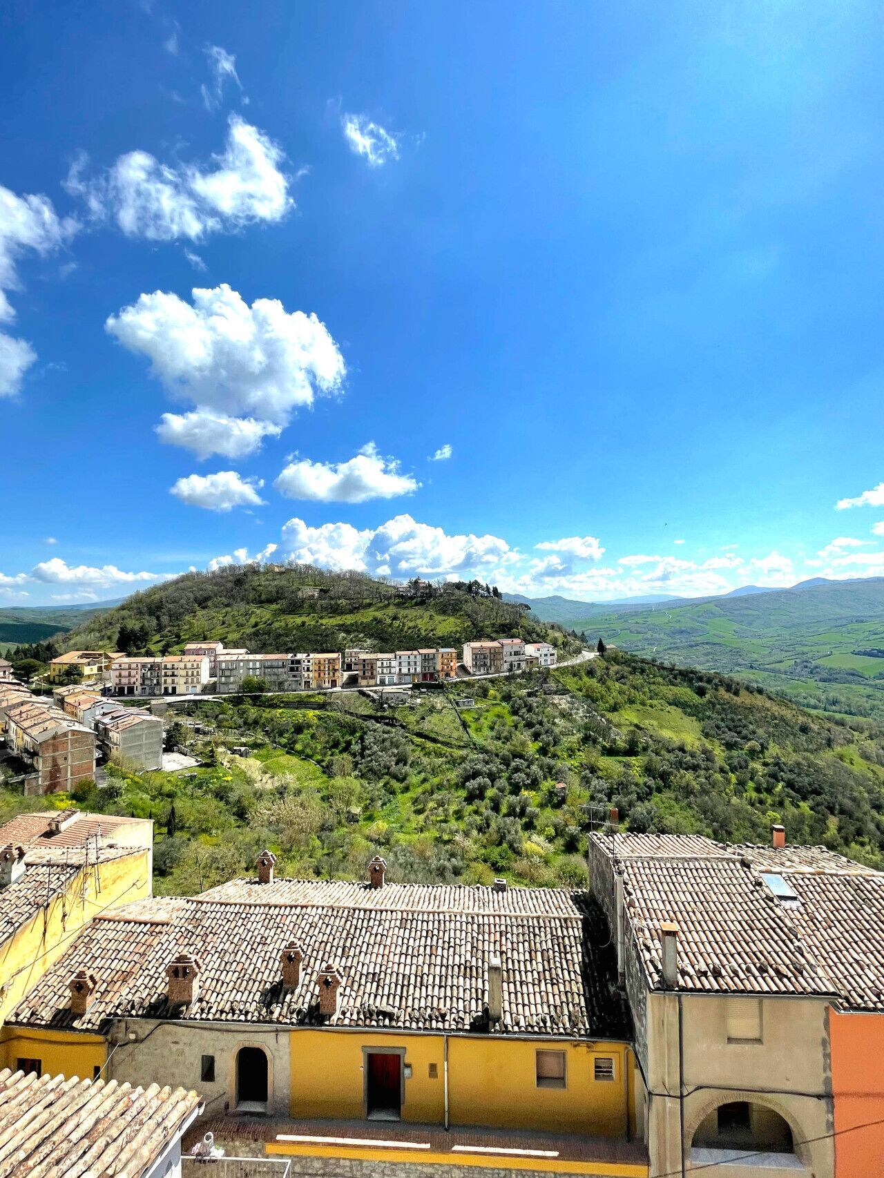 A hillside village with terracotta-roofed buildings, a prominent church, and a view of the surrounding countryside.