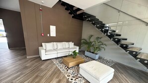 A modern living room with a white sofa, a wooden coffee table, a patterned rug, and a potted plant. A staircase with a glass railing leads to an upper level. - Edificio Lotus - Torices (Cartagena)