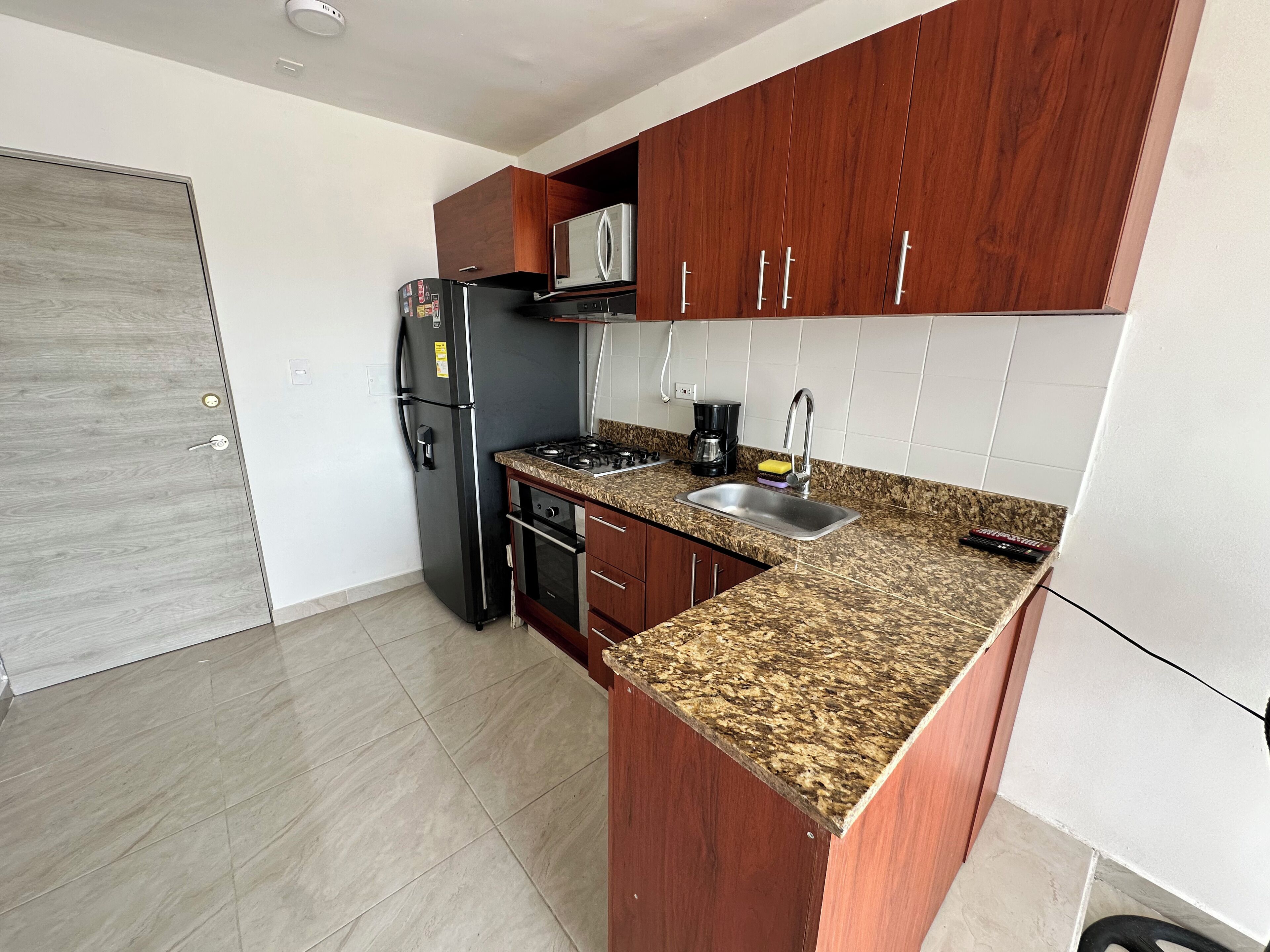 A compact kitchen with a refrigerator, stove, sink, and wooden cabinets.