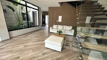 Uma sala de estar espaçosa com um sofá branco, uma mesa de centro e uma escada de vidro.