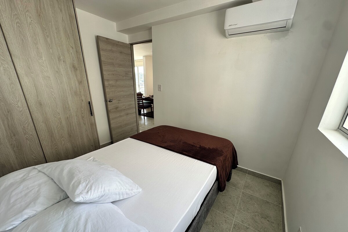 Quarto com cama, guarda-roupa, colcha castanha e ar condicionado.