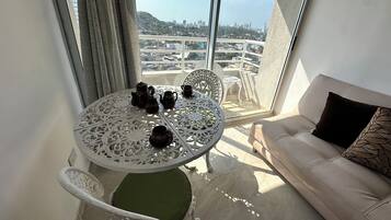 Uma varanda com uma mesa posta com bules e xícaras, um sofá e vista para o horizonte urbano.