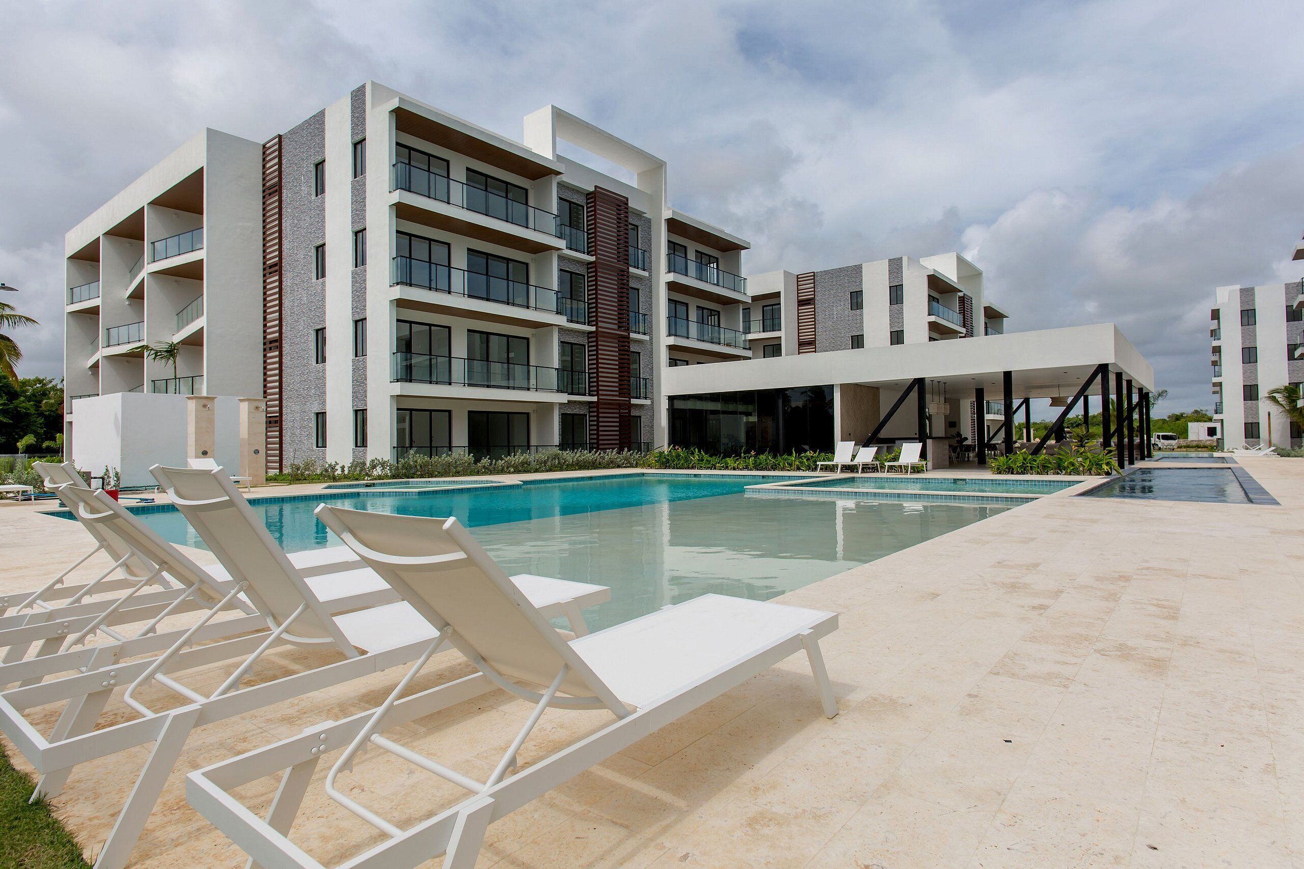 A modern hotel with a swimming pool, multiple balconies, and sun loungers.