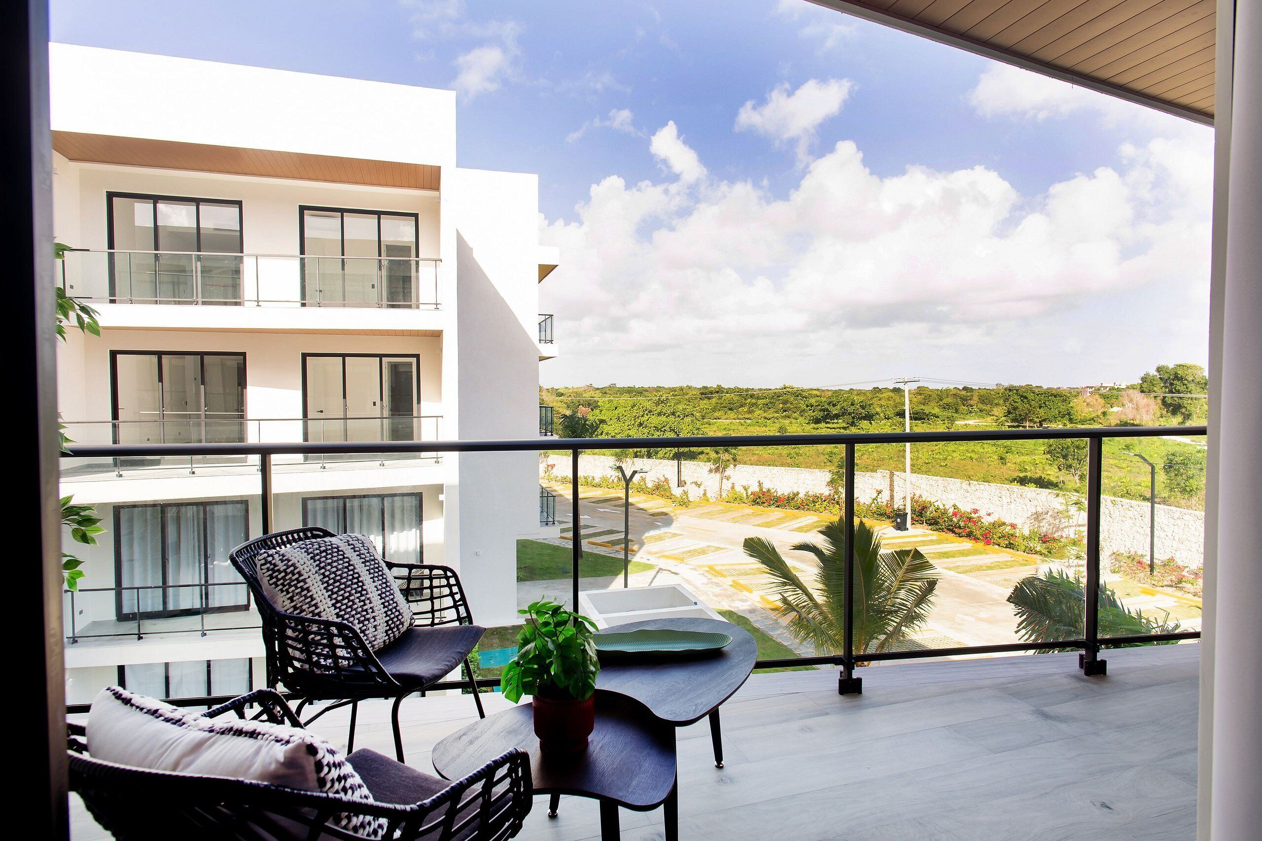 A balcony with a view of a landscaped area, a table with chairs, and a potted plant.