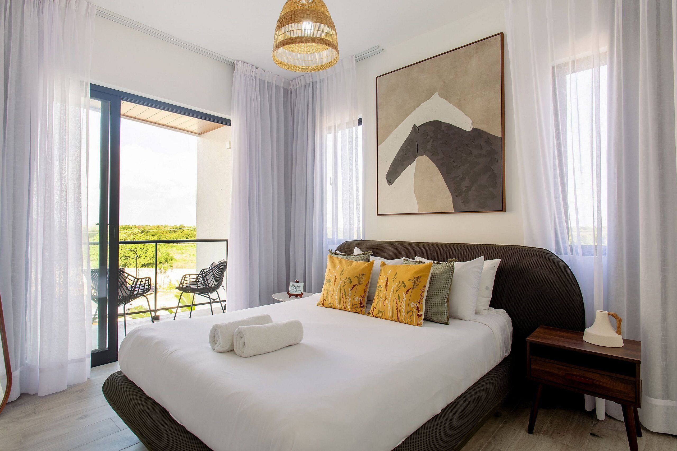 Une chambre spacieuse avec un grand lit, un balcon avec des chaises et un tableau au mur.
