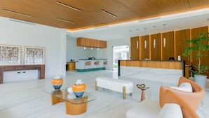 A modern reception area with a wooden reception desk, seating, and a glass coffee table with decorative vases. - 1BR apartment pool, golf, and artificial beach (Punta Cana)